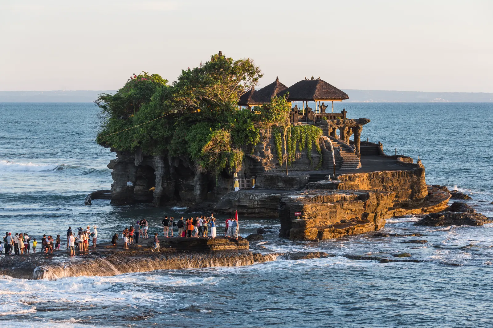 Tanah Lot tempel op een rots in zee bij zonsondergang, met bezoekers op de rotsen ervoor