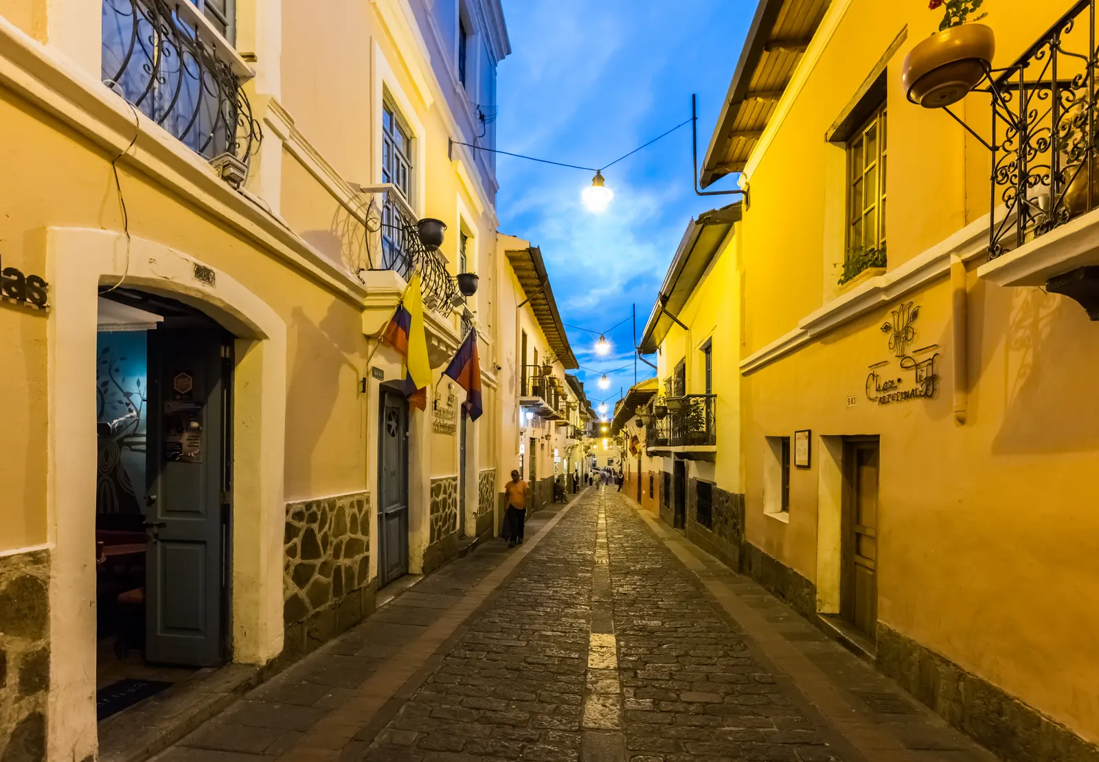 Smalle kasseienstraat Calle La Ronda in Quito met gele koloniale huizen, balkons en vlaggen in de avondschemering