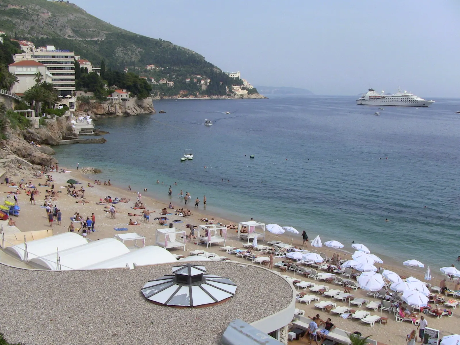 Banje strand in Dubrovnik met ligbedden, parasols en helderblauwe zee, op de achtergrond een cruiseschip