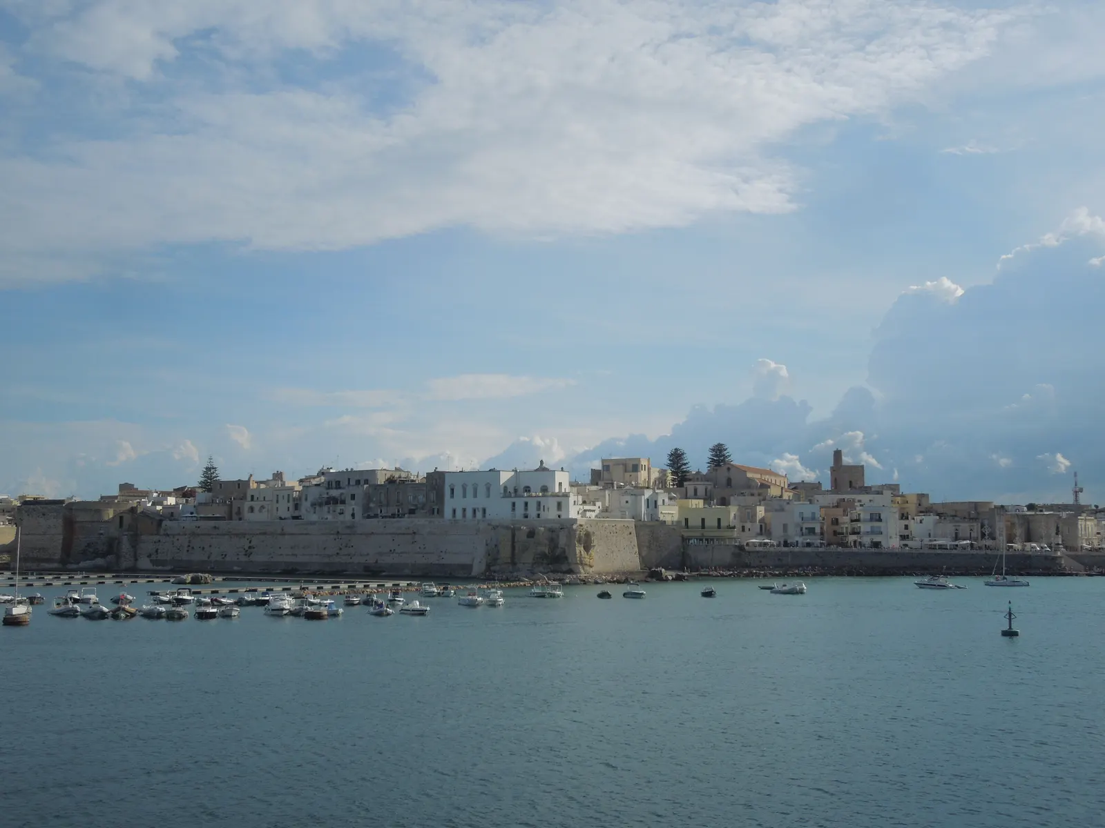 Witte huizen en stadsmuren van het historische centrum van Otranto aan zee, met bootjes in de haven