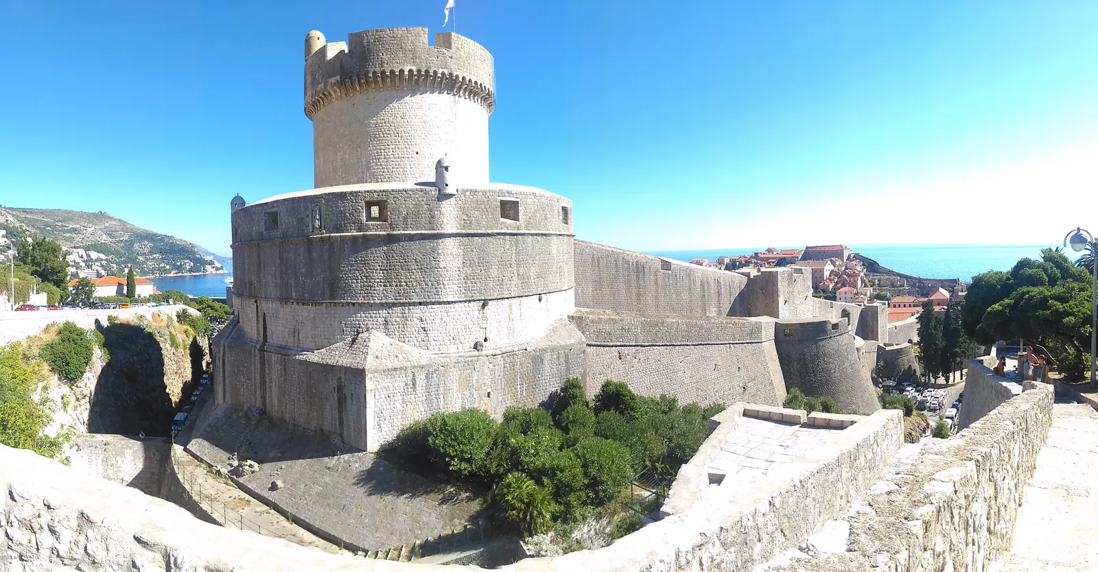 De ronde Minčeta-toren op de stadsmuur van Dubrovnik onder een strakblauwe lucht, met zee op de achtergrond