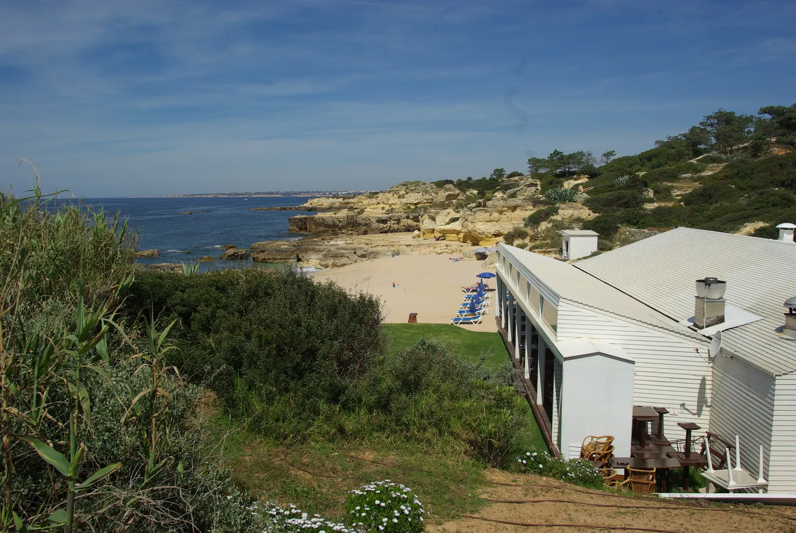 Zandstrand Praia do Evaristo met strandbedden, rotsen en groene kliffen naast een wit strandrestaurant