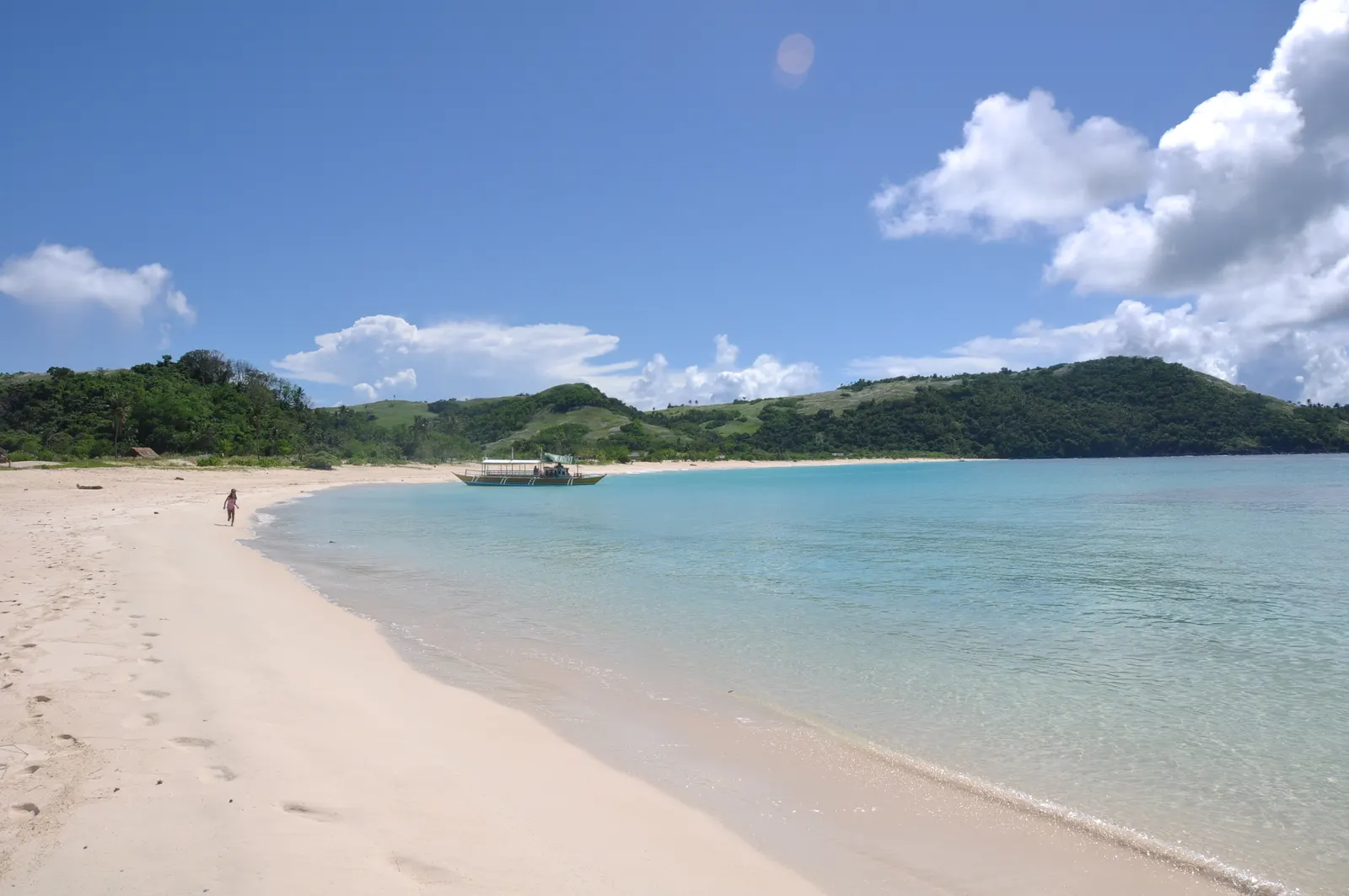 Wit zandstrand met turquoise water en groene heuvels op Calaguas, met een bangka-boot in de baai