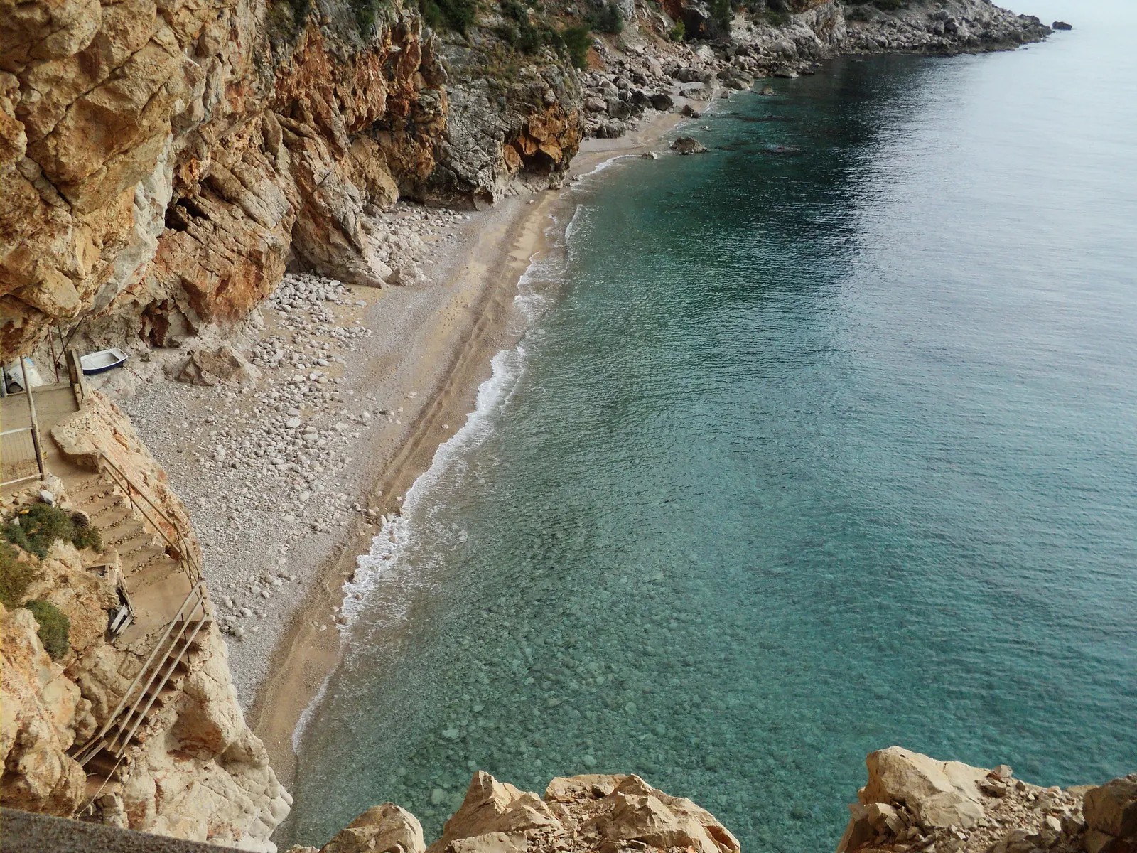 Kiezelstrand van Pasjača onder steile rotskliffen met helder turquoise water, van bovenaf gezien