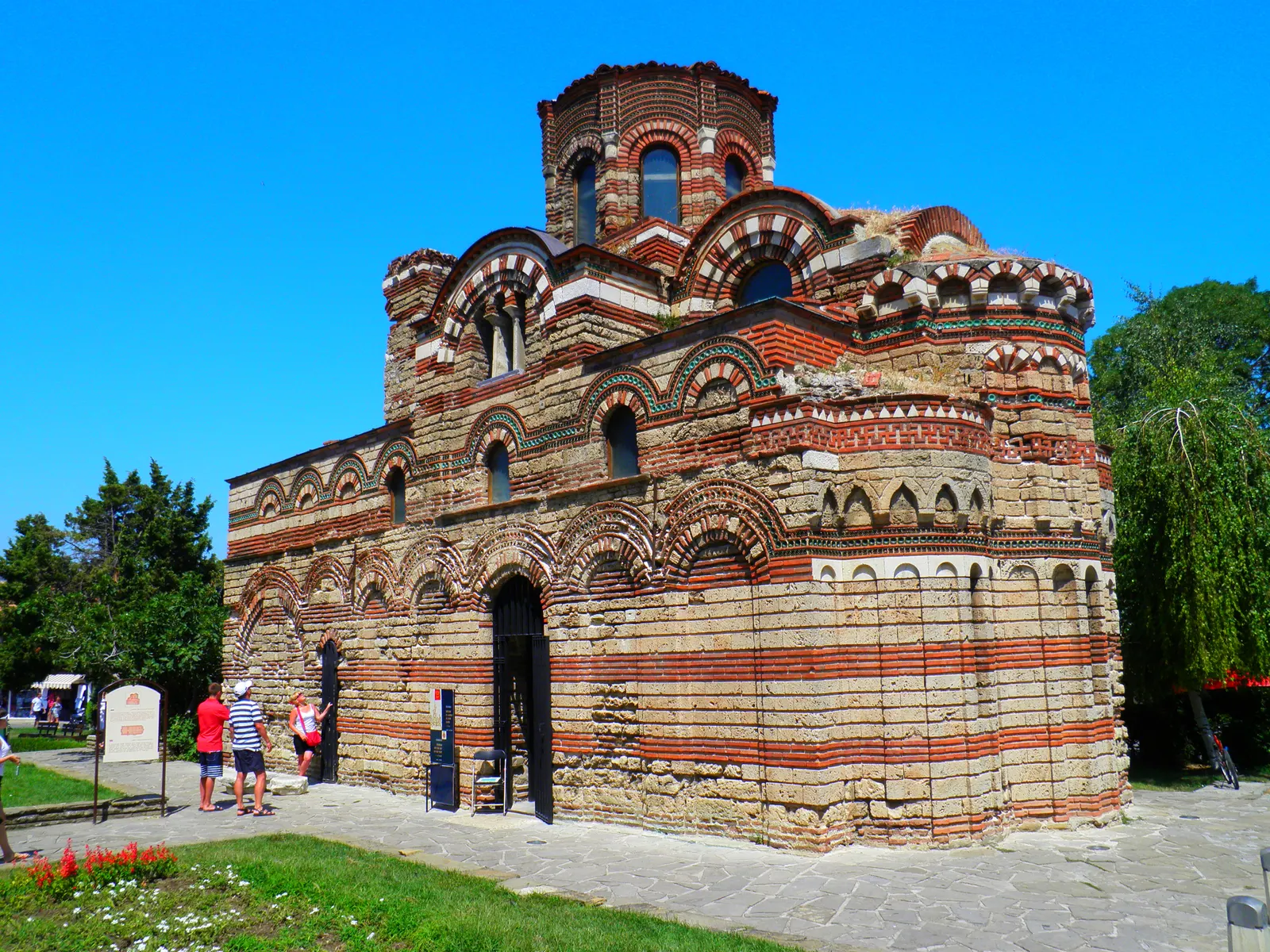 Kerk van Christus Pantocrator in Nessebar met rood-wit gestreept metselwerk en koepeltoren onder blauwe lucht