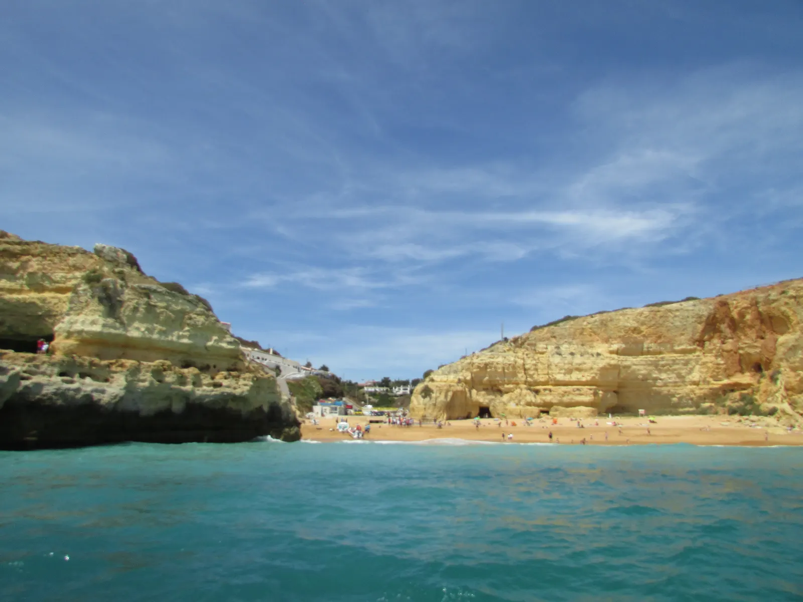 Strand van Benagil vanaf zee gezien, met gele kliffen, turquoise water en het dorpje op de achtergrond