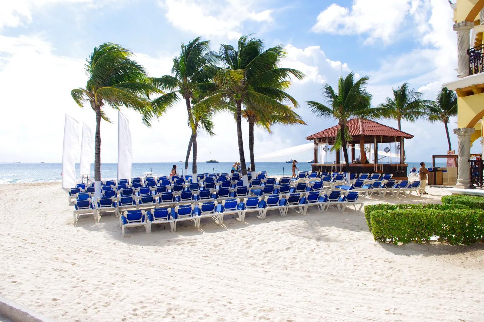 Wit zandstrand met blauwe ligbedden, palmbomen en een paviljoen aan zee bij een resort in Playa del Carmen