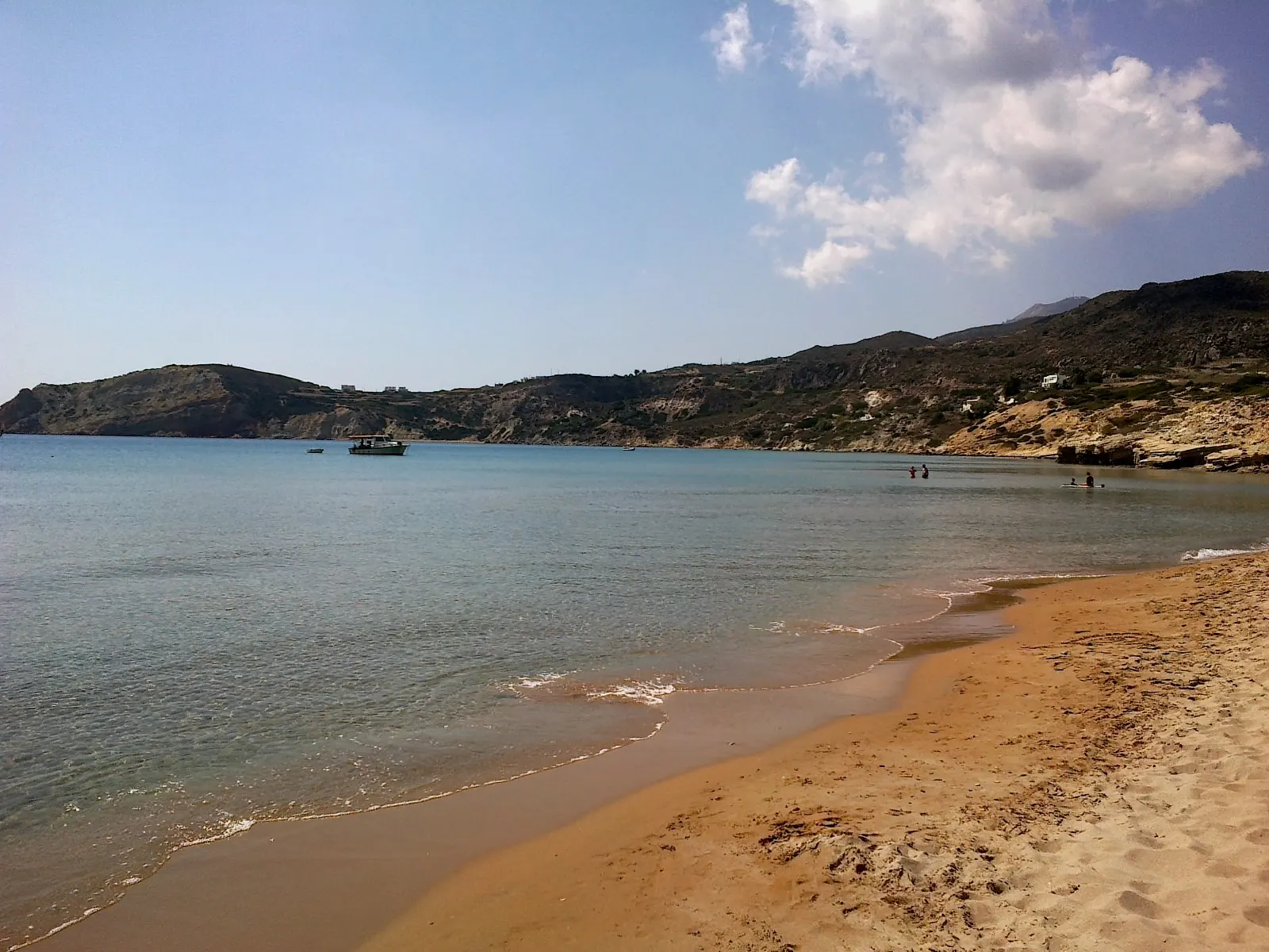 Breed goudkleurig zandstrand van Provatas met kalme zee, een bootje en heuvels op Milos