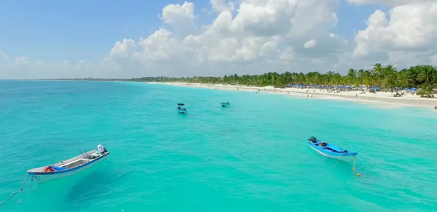Turquoise zee met drie bootjes voor een wit strand met palmbomen bij Playa Paraiso in Tulum