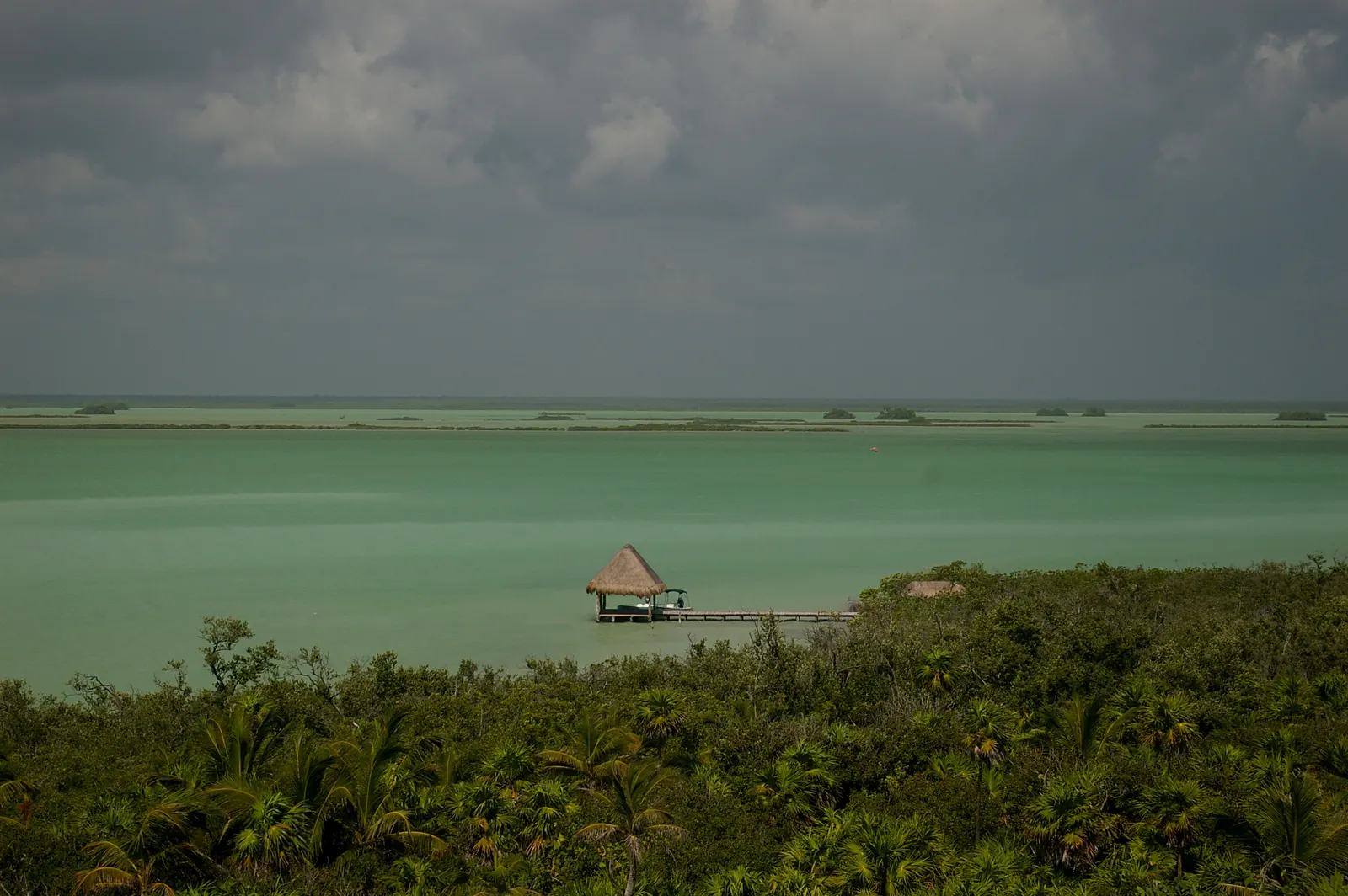 Turquoise lagune met palapa-steiger tussen tropisch groen onder donkere wolken in Sian Ka'an