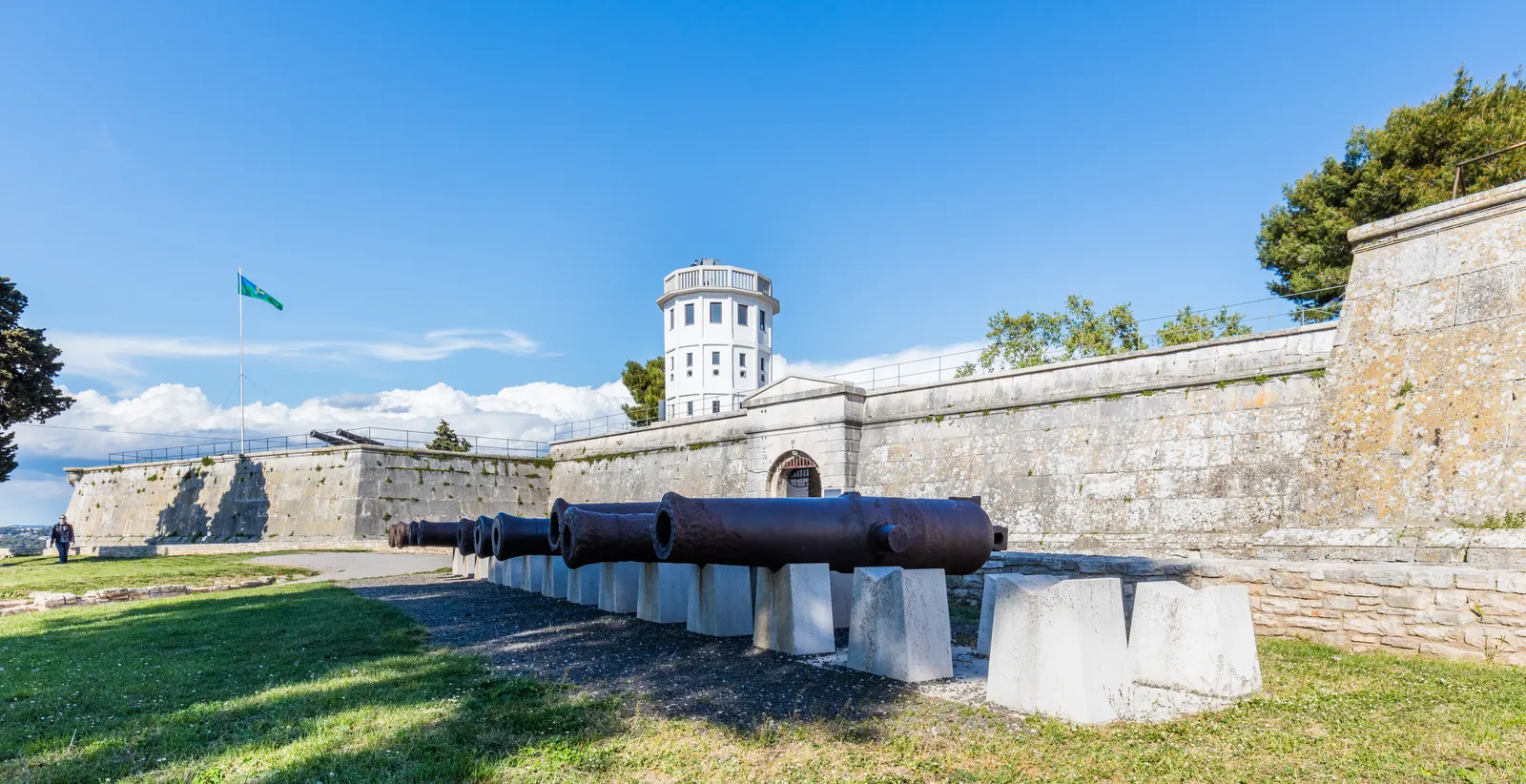 Vestingmuren van het Kastel in Pula met oude kanonnen, een witte toren en een vlag onder een blauwe lucht