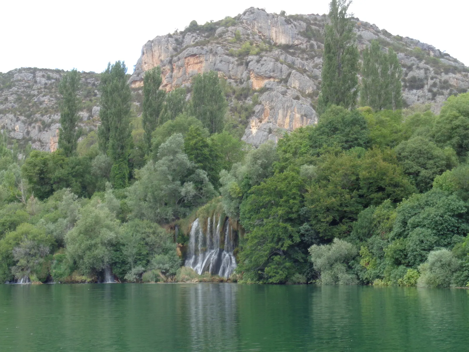 Roški Slap: watervallen tussen groene bomen aan een meer, met kalkstenen rotswanden op de achtergrond
