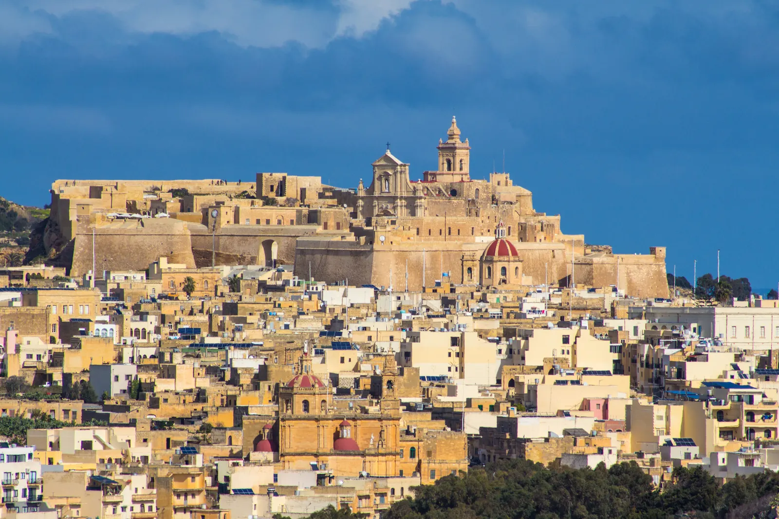 De Citadel van Victoria met kathedraal boven de okerkleurige huizen van Victoria op Gozo, onder een donkerblauwe lucht