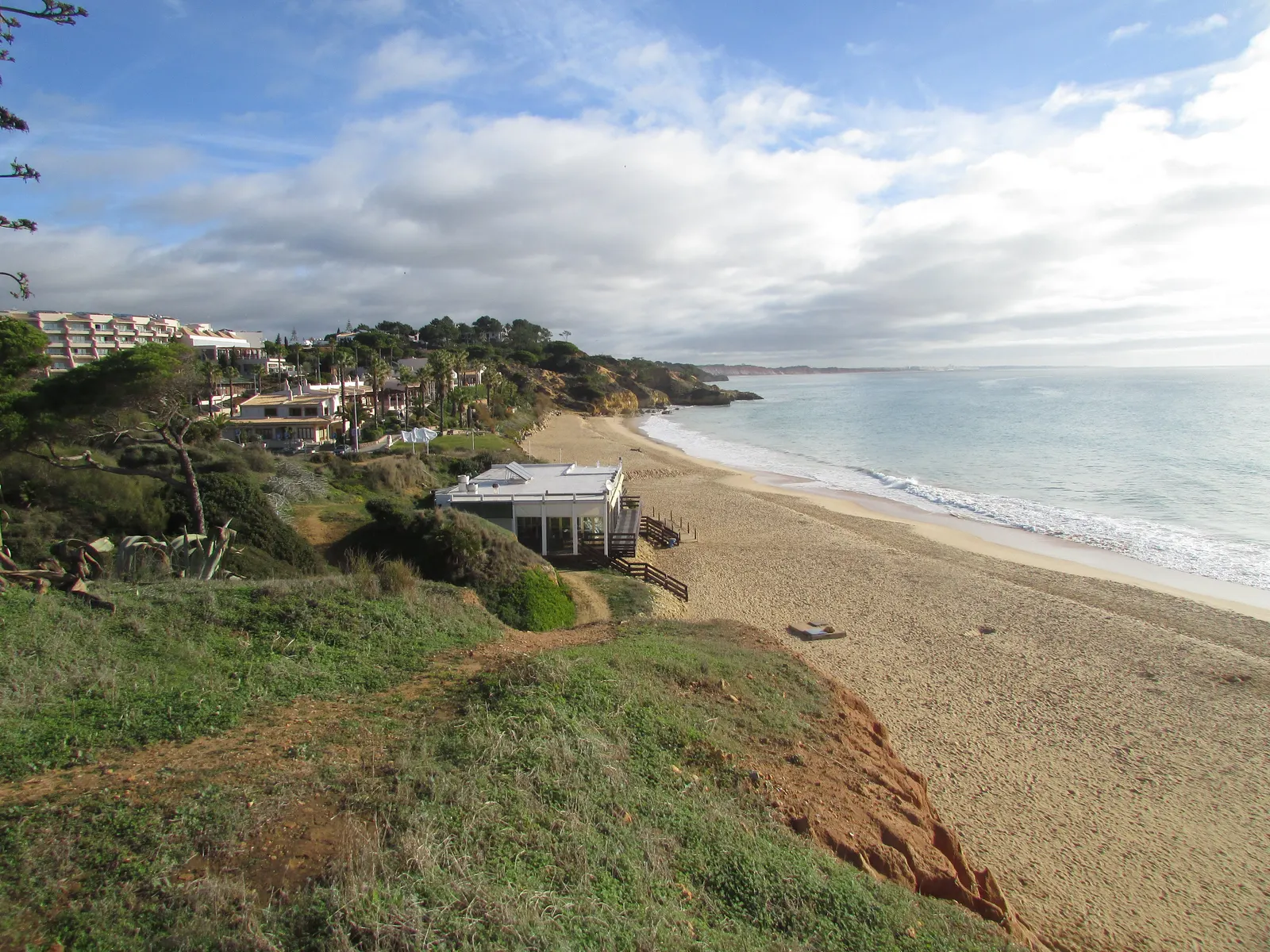 Zandstrand van Praia de Santa Eulália met strandpaviljoen, groene kliffen en hotels langs de kust