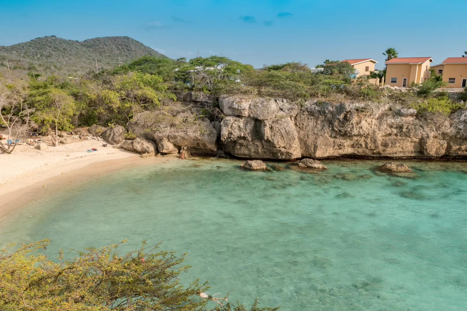 Zandstrand van Playa Lagun met turquoise water tussen rotsachtige kliffen en groene heuvels op Curaçao