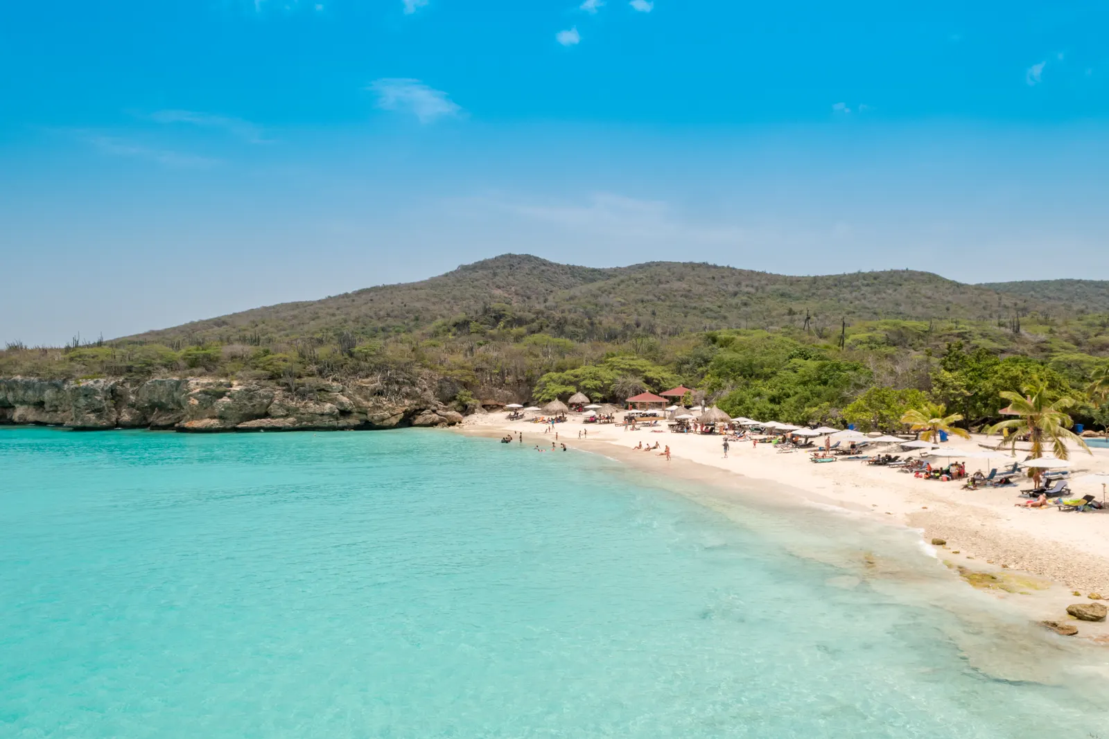 Wit zandstrand van Grote Knip met turquoise zee, rotskust en groene heuvels onder een blauwe lucht