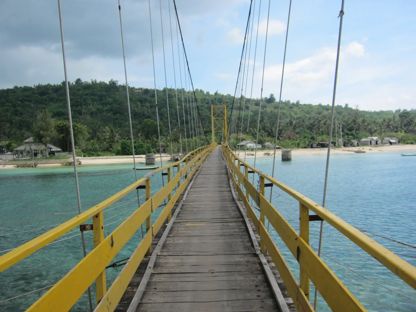 Gele hangbrug van planken over turquoise water naar het groene, beboste Nusa Ceningan