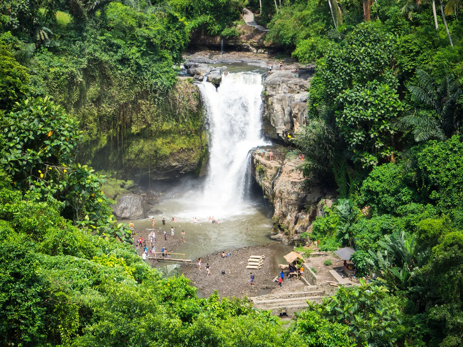 Tegenungan waterval in Bali, omringd door groene jungle met bezoekers bij het meertje eronder
