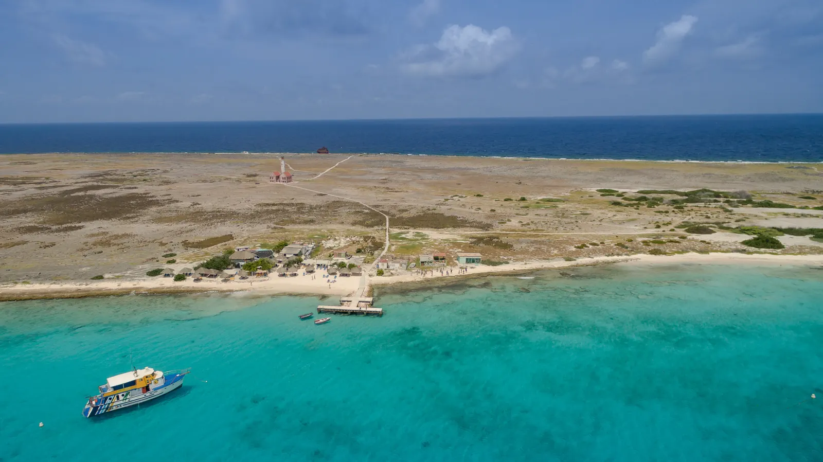 Luchtfoto van Klein Curaçao met wit strand, steiger, boot in turquoise water en de vuurtoren op de achtergrond