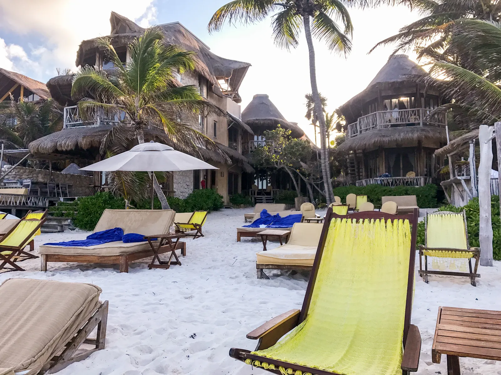 Strandbedjes en ligstoelen op wit zand voor rieten bungalows en palmbomen van Alaya Tulum