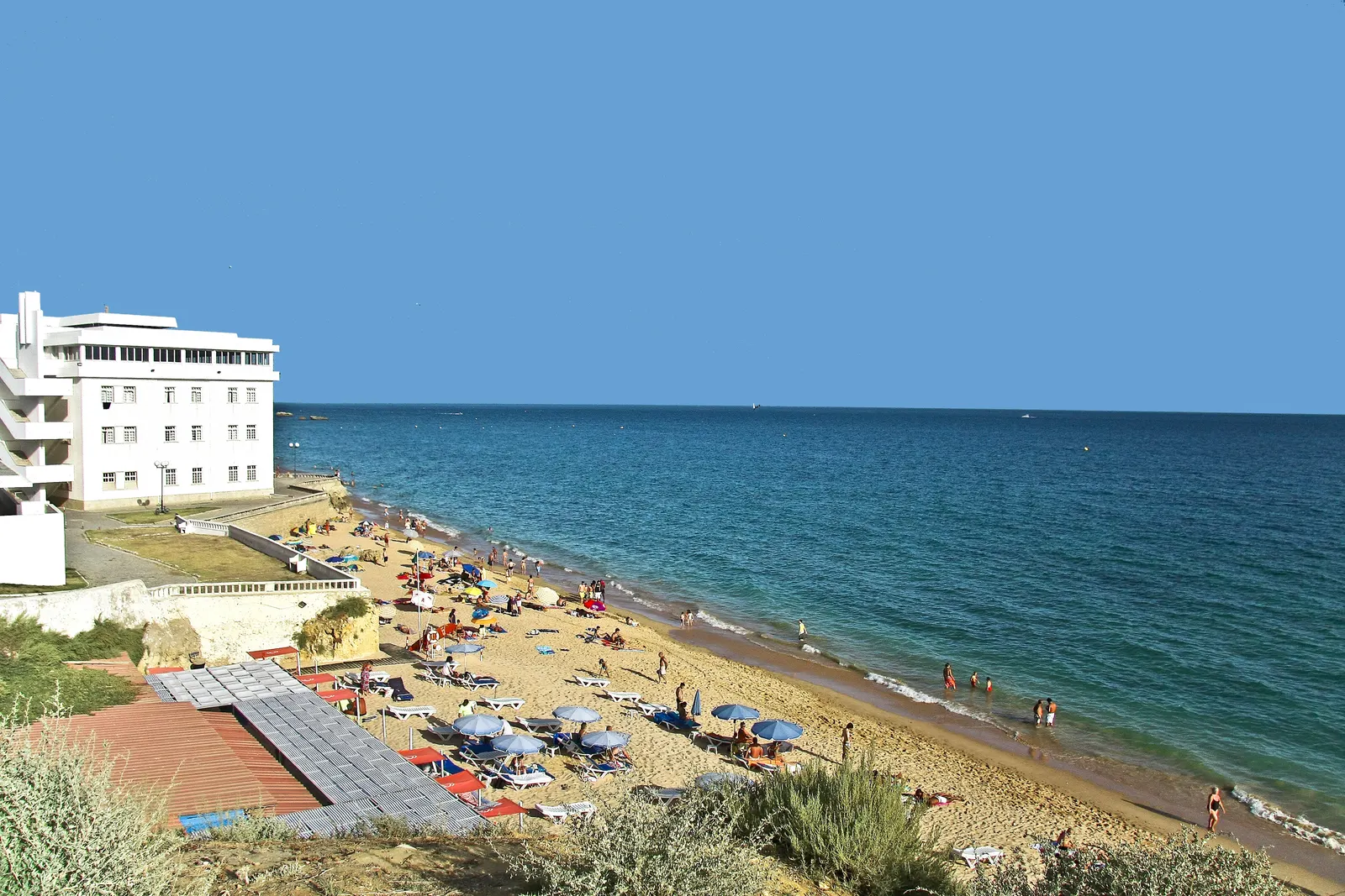 Zonnig zandstrand met parasols en ligbedden naast een wit hotel aan de blauwe zee bij Albufeira