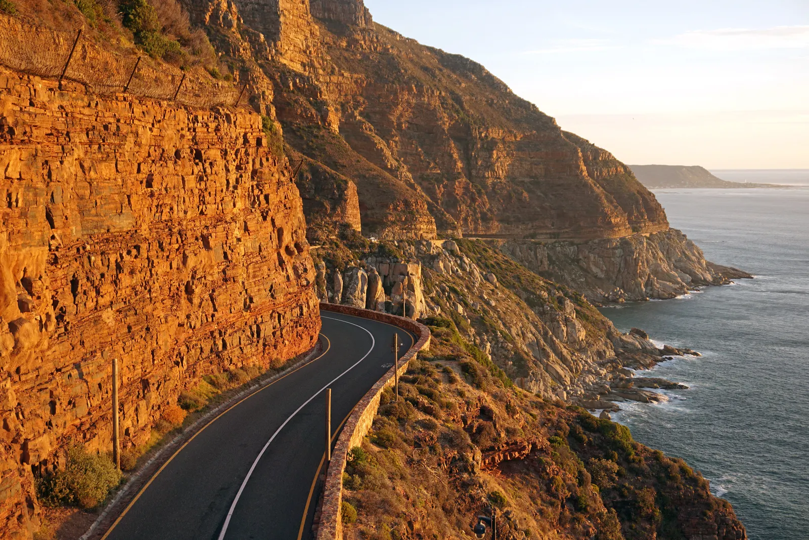 Kronkelende kustweg Chapman's Peak Drive langs oranje rotswanden en de oceaan bij zonsondergang