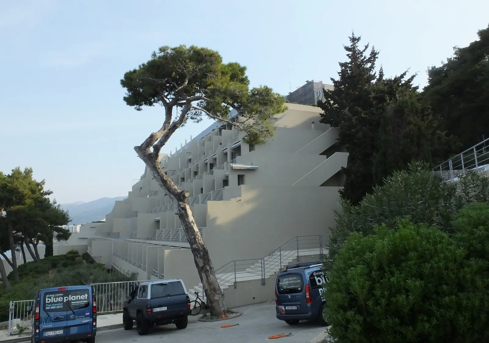 Terrasvormige gevel van Hotel Dubrovnik Palace tussen pijnbomen op een heuvel aan de kust