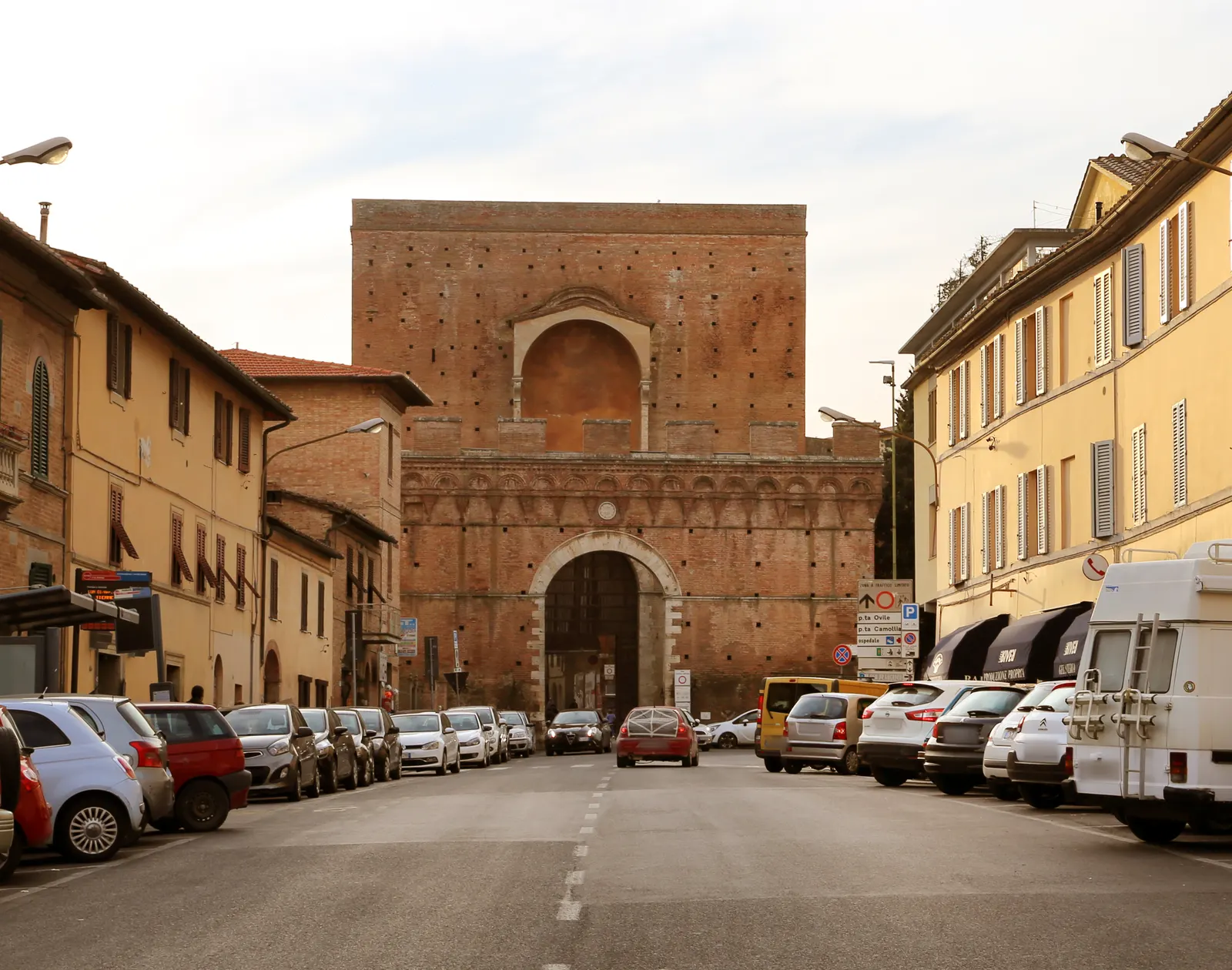 Bakstenen stadspoort Porta Pispini in Siena met boognis, gezien vanaf een straat met geparkeerde auto's