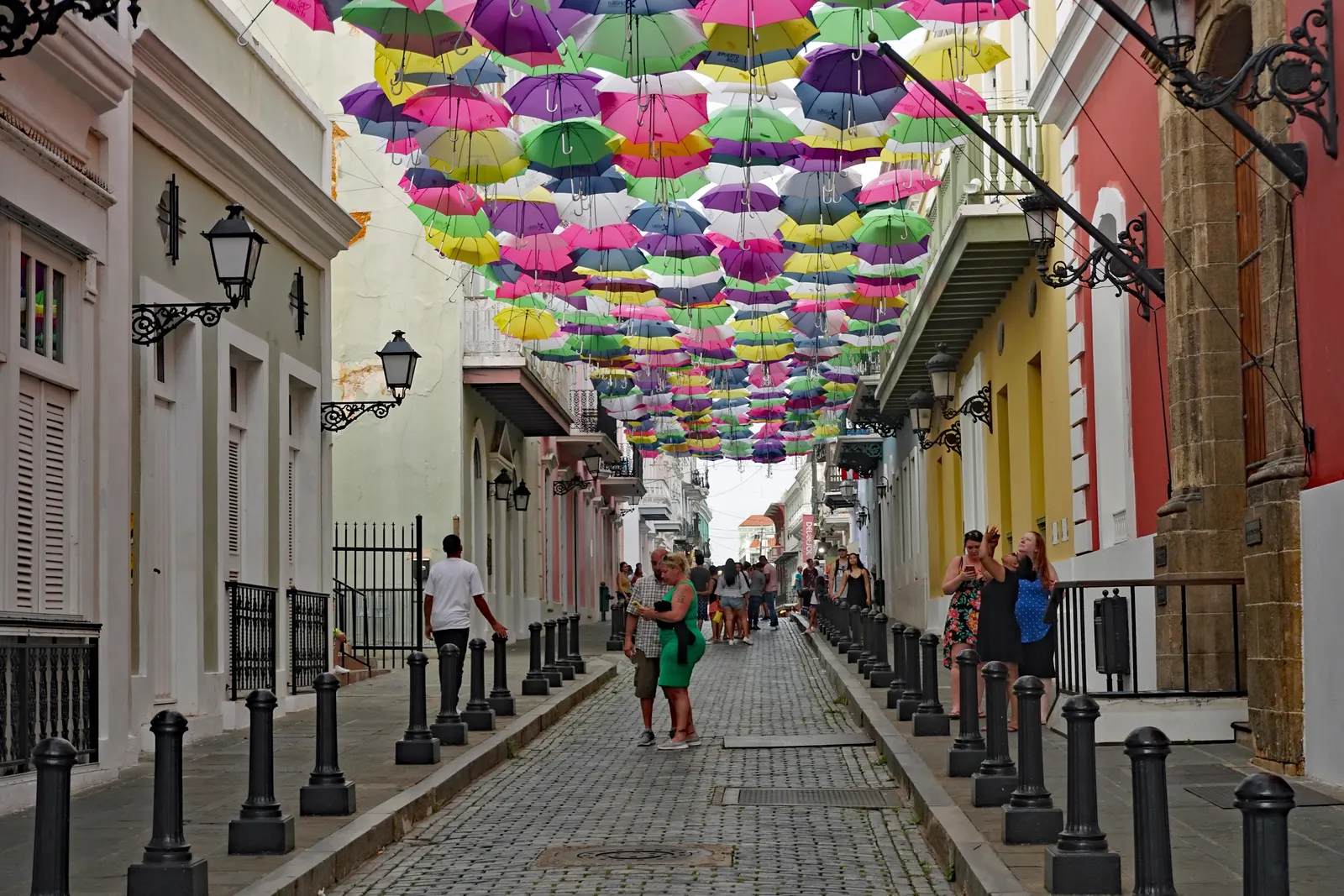 Kleurrijke paraplu's boven een straat met kasseien en pastelkleurige koloniale gevels in Old San Juan