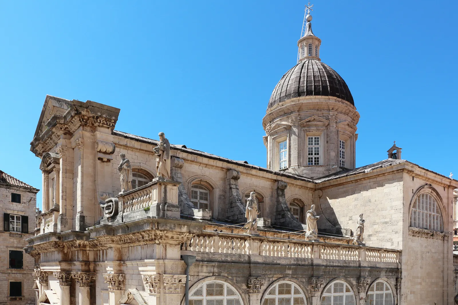 Barokke kathedraal van Dubrovnik met grote koepel en beelden op de balustrade onder een strakblauwe lucht