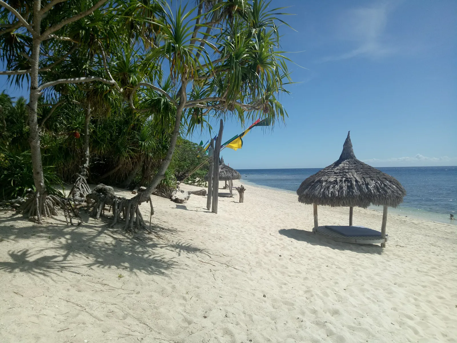 Wit zandstrand met palmbomen en een rieten parasol aan een helderblauwe zee op Siquijor