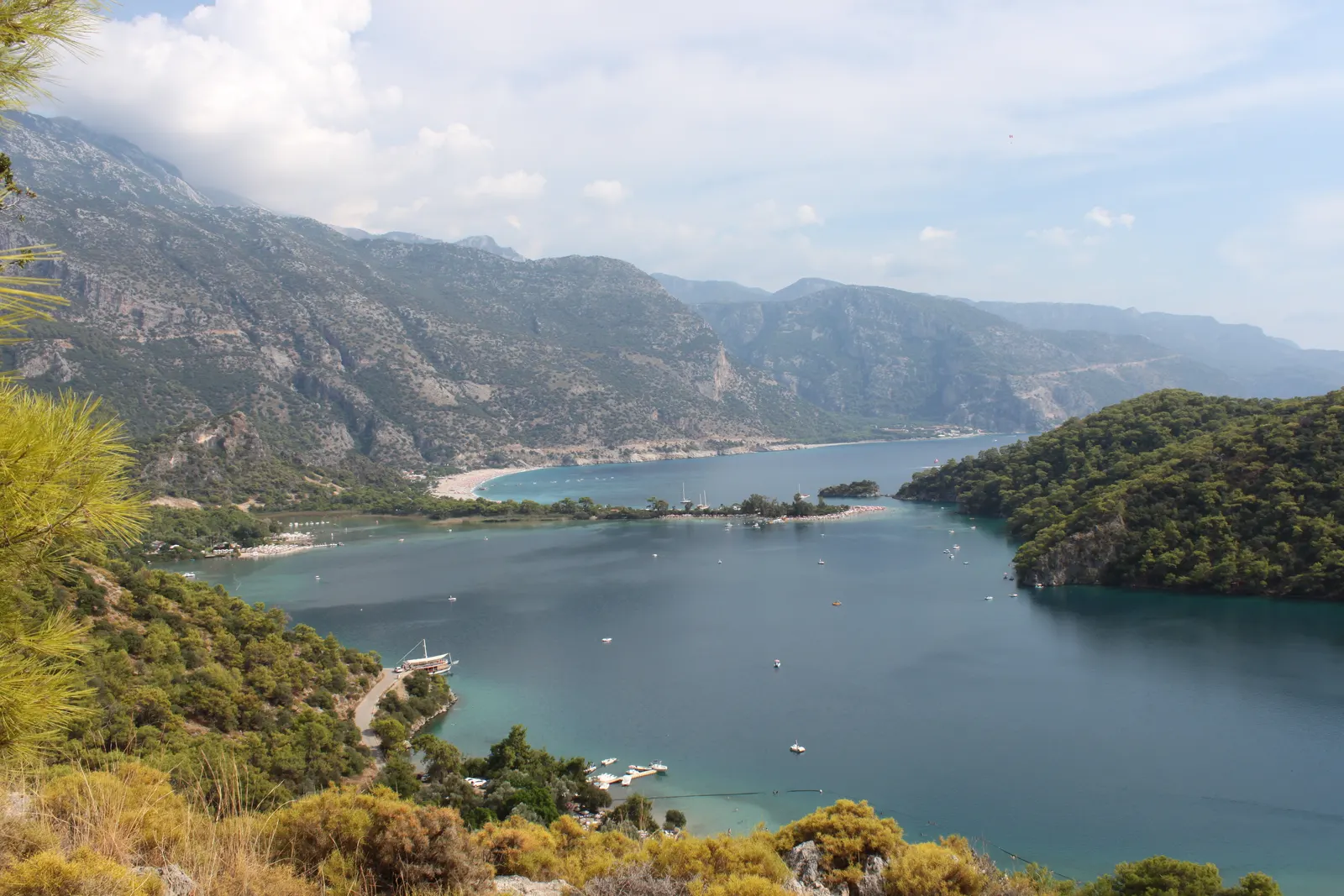 Uitzicht over de lagune van Ölüdeniz met turquoise water, boten, beboste heuvels en bergen op de achtergrond