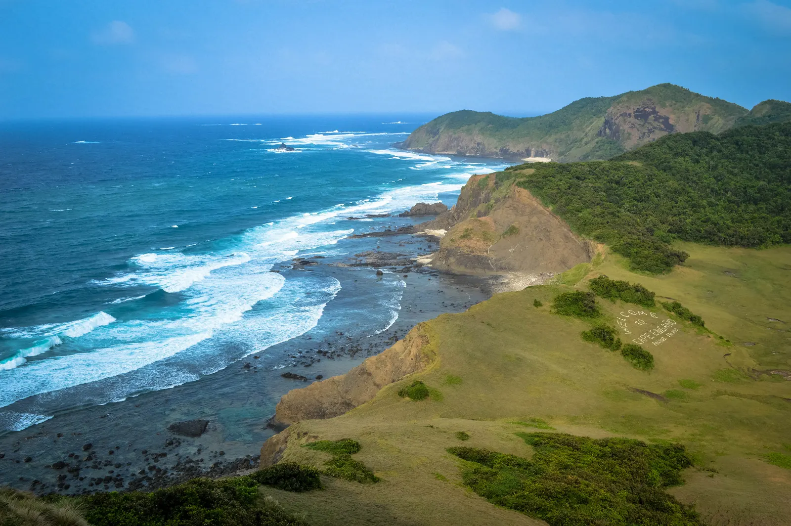 Groene heuvels en kliffen langs de woeste kust van Palaui Island met witte golven op een blauwe zee