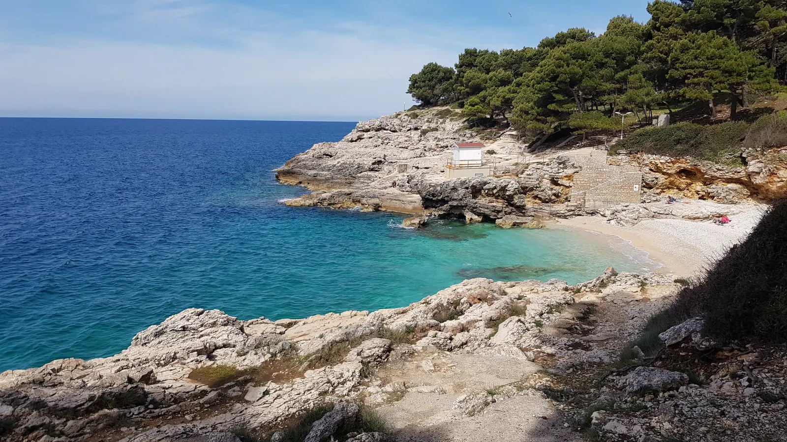 Rotsachtige baai met turquoise water en een klein kiezelstrand onder pijnbomen aan de kust bij Pula