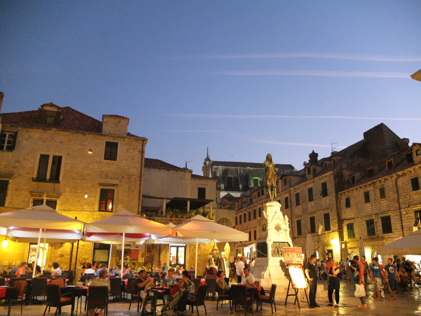 Gundulić-plein in Dubrovnik bij schemering met terrassen, parasols en het standbeeld van Gundulić